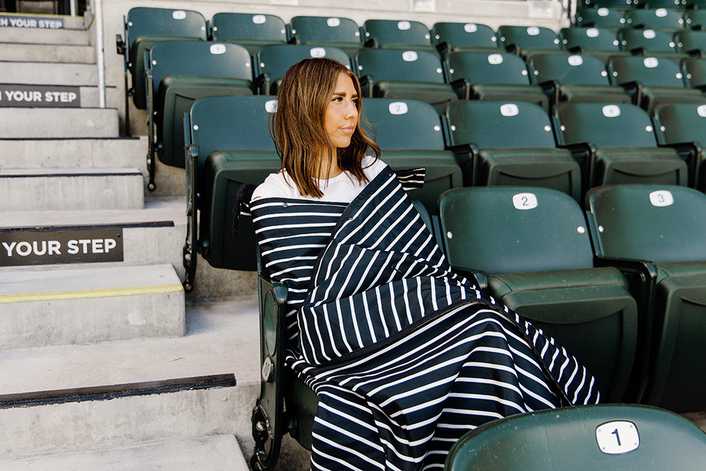 A woman sitting in a baseball stadium wrapped in a black and white striped blanket.