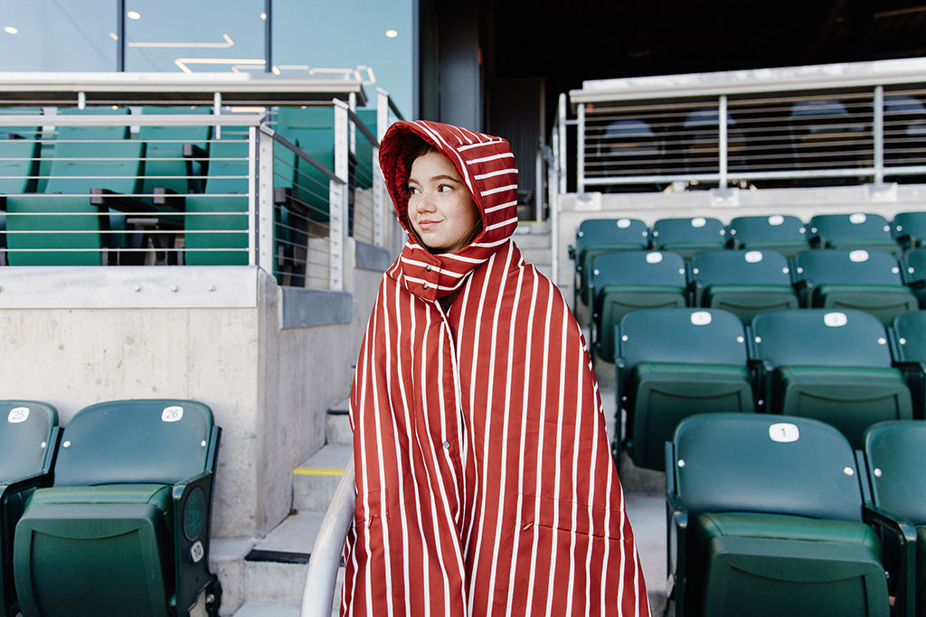 A woman standing in a baseball stadium wrapped in a maroon and white striped blanket.