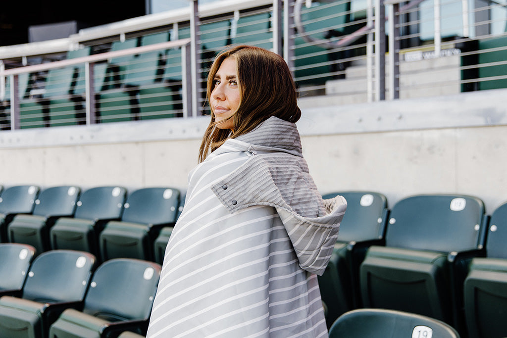 A woman standing in a baseball stadium wrapped in a grey and white striped blanket.