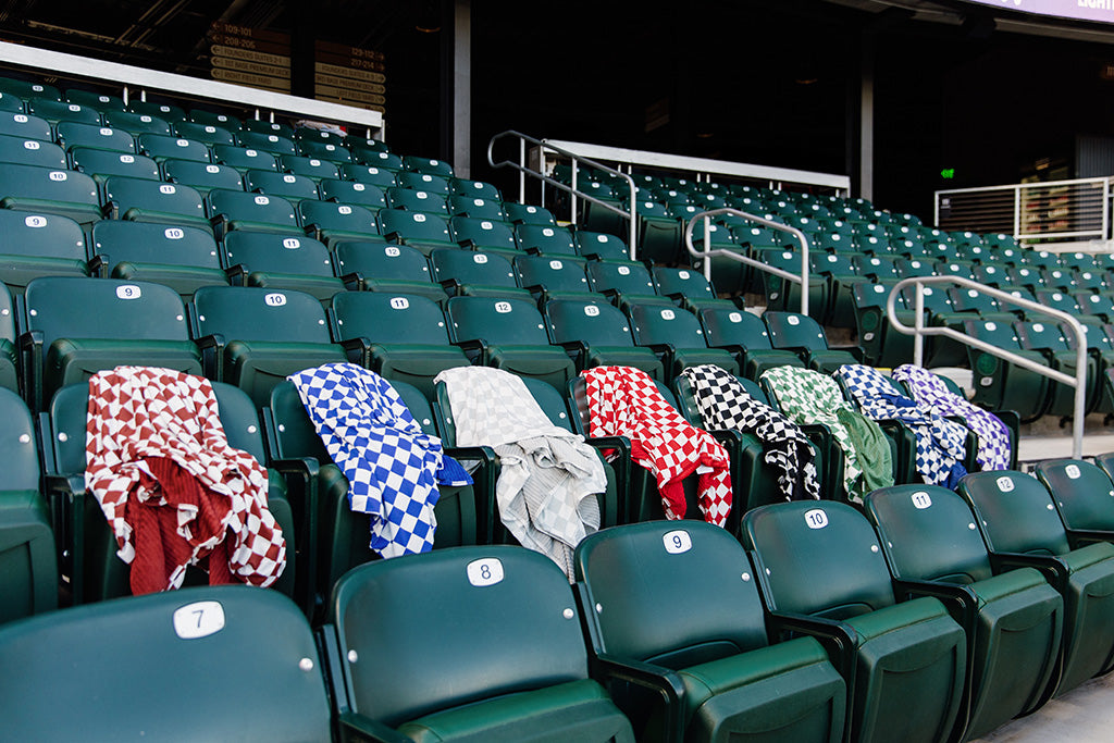 Different colored check patterned blankets  lying on green seats in a baseball stadium. 
