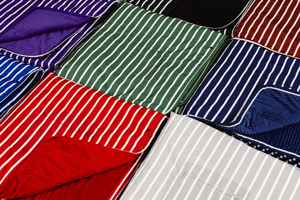 Different colored striped blankets folded and placed next to each other on the floor.