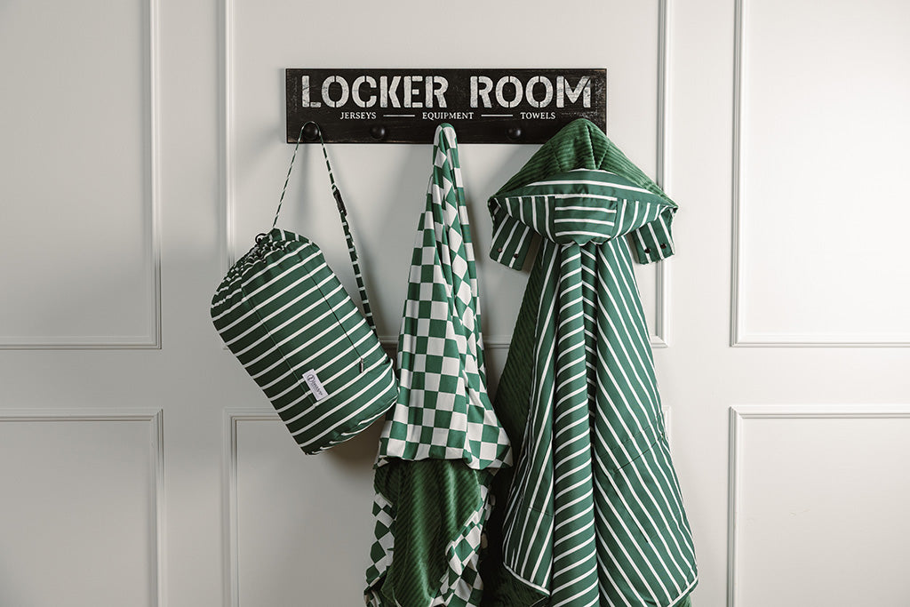 A green and white striped stadium blanket and bag and green and white check blanket hanging on a decorative wall hanger. 