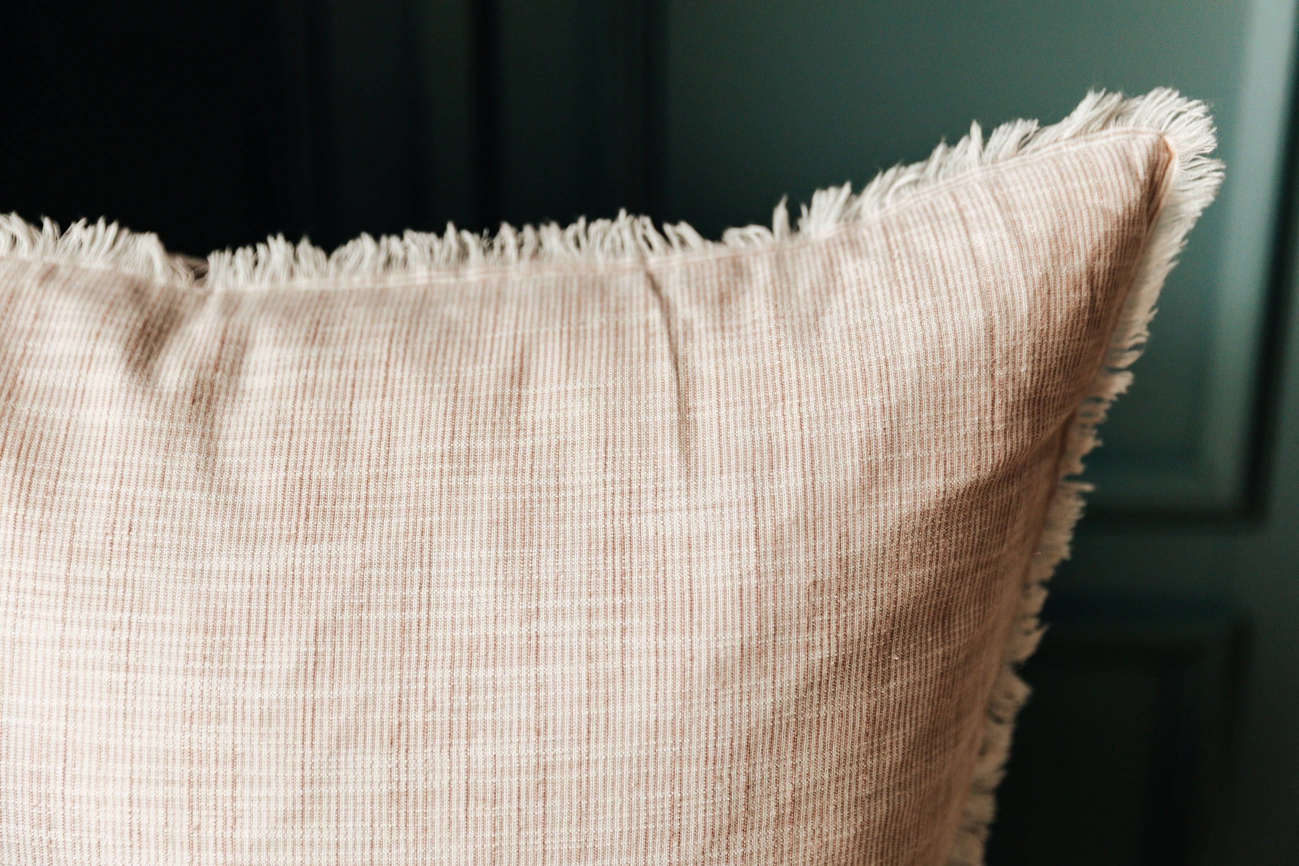A close up corner view of a light pink woven striped euro pillow and its' frayed edges.