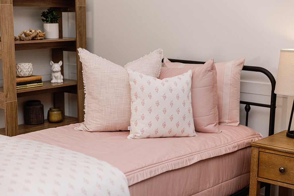 Twin bed with pink knitted zipper bedding with pink, cream, and white accessories.