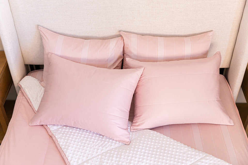 A bed made with pink zipper bedding with the comforter pulled back and pillows on top of the bed.