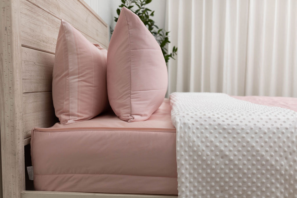 A side view of a pink zipper bedding on a bed with the top unzipped halfway down revealing the minky comfort interior. 