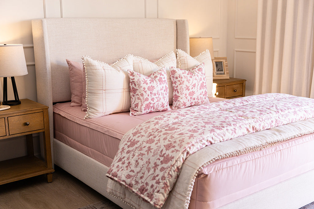 A bed made with pink zipper bedding and an assortment of pink floral and white tassel pillows and blanket.