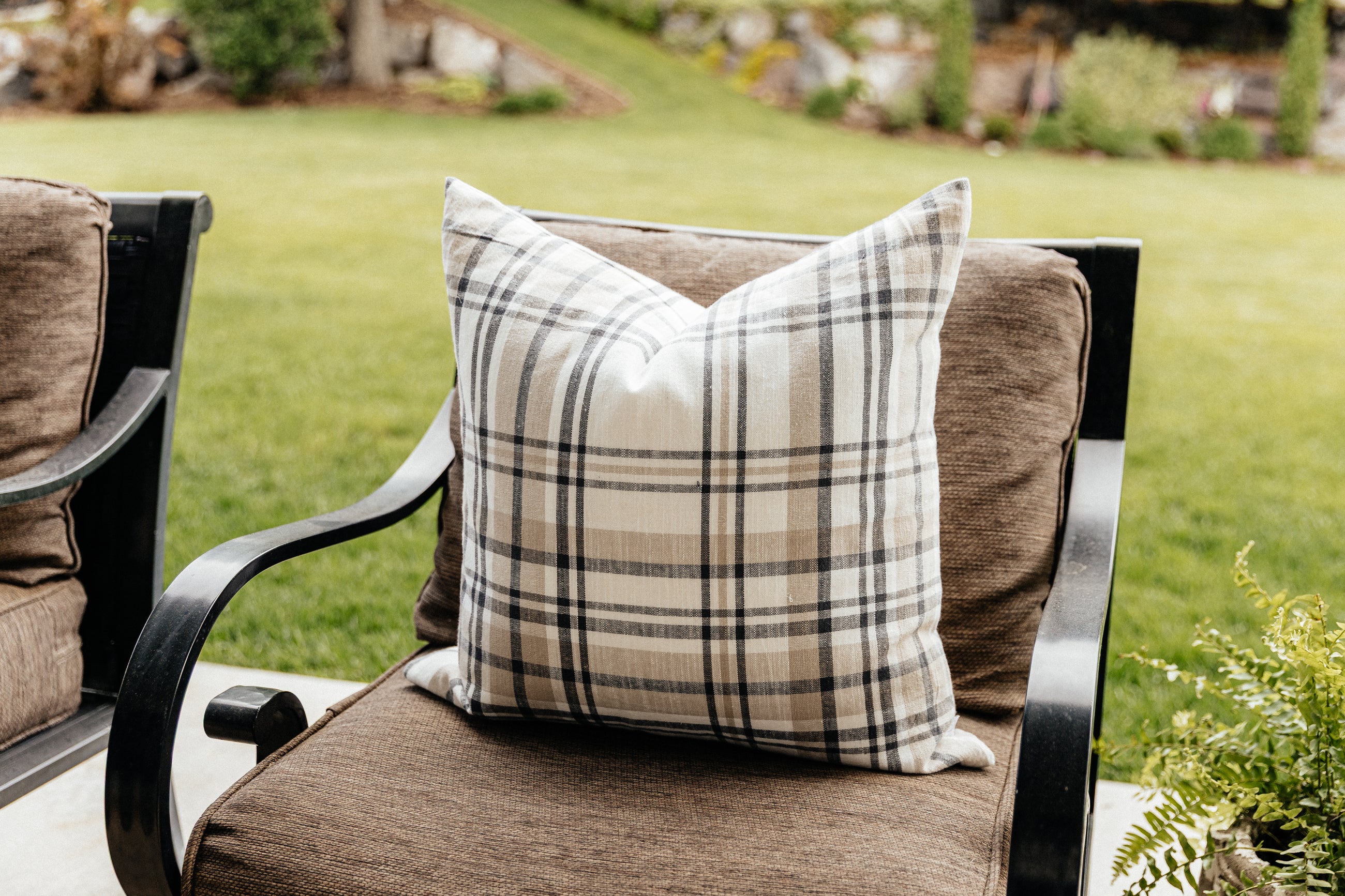 A charcoal, cream, and tan plaid euro pillow on a chair outside.