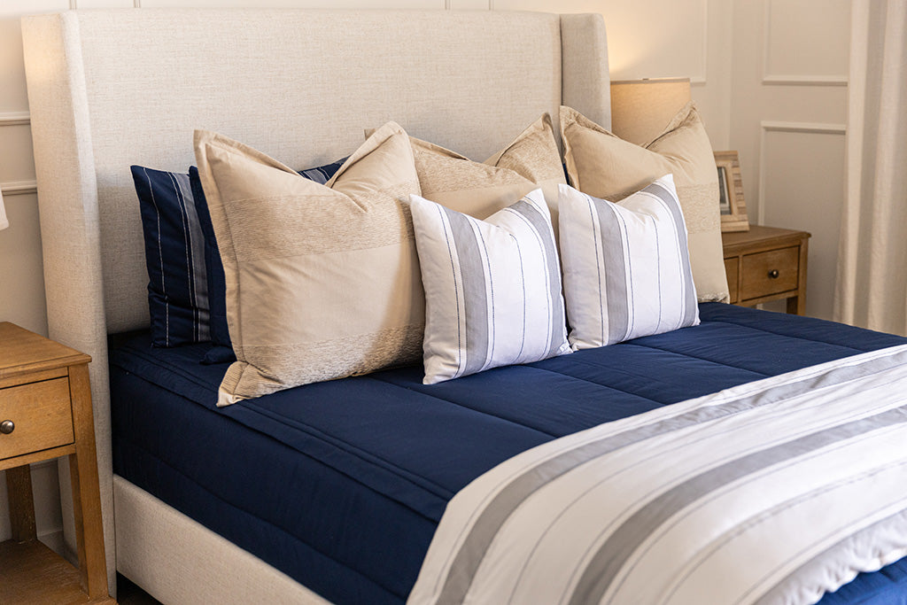 A bed made with navy blue zipper bedding and an assortment of neutral and striped throw pillows and blanket.