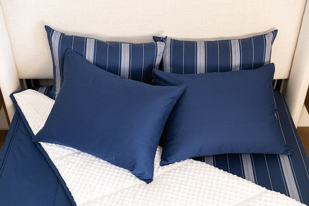 A bed made with navy blue zipper bedding with the comforter pulled back and pillows on top of the bed.