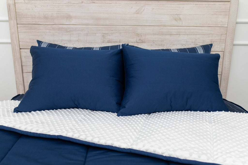 Navy blue zipper bedding on a bed with the comforter pulled back and pillows on top.