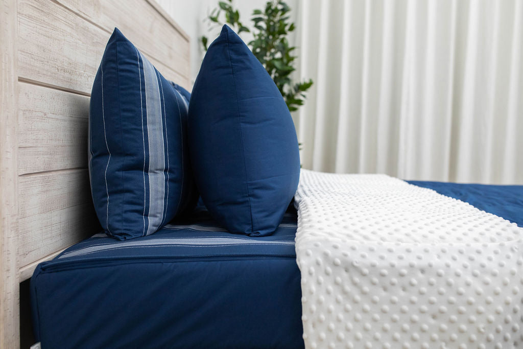 A side view of a navy zipper bedding on a bed with the top unzipped halfway down and the comforter folded down.