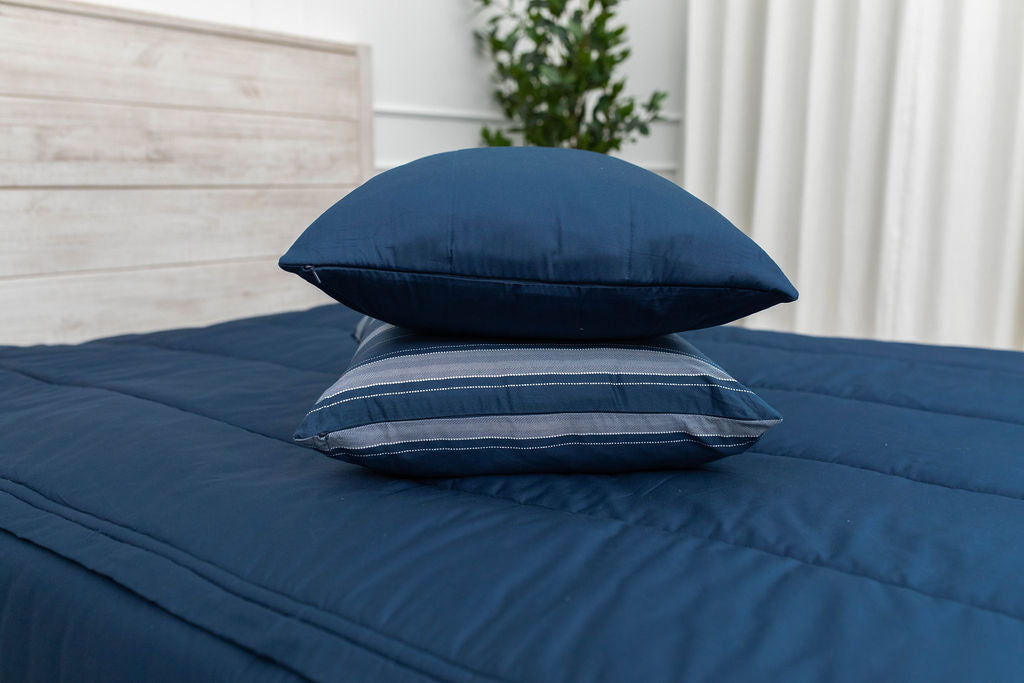 Navy blue pillows in the middle of a made bed on top of the matching zipper bedding. 