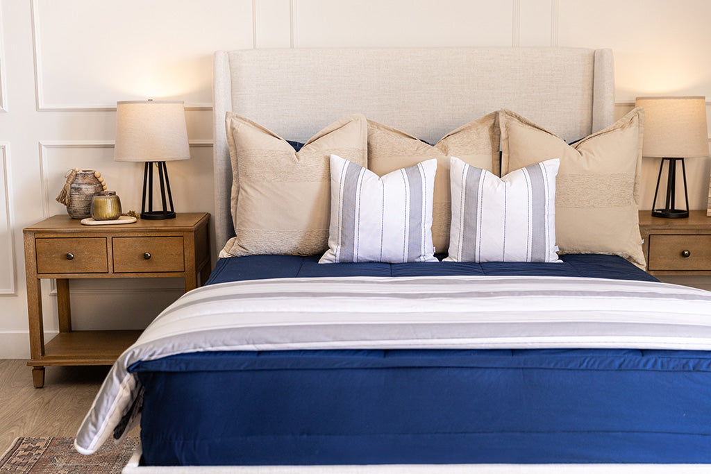 A bed made with navy blue zipper bedding and an assortment of neutral and striped throw pillows and blanket.