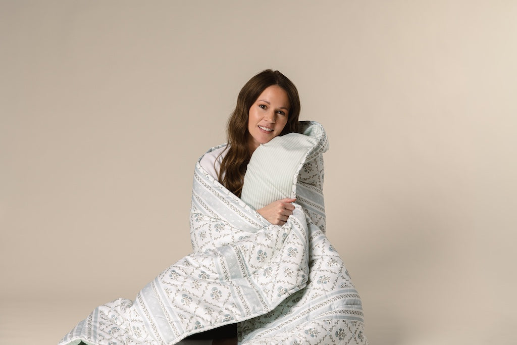 A model wrapped a blue floral and light blue corduroy blanket on a cream backdrop.