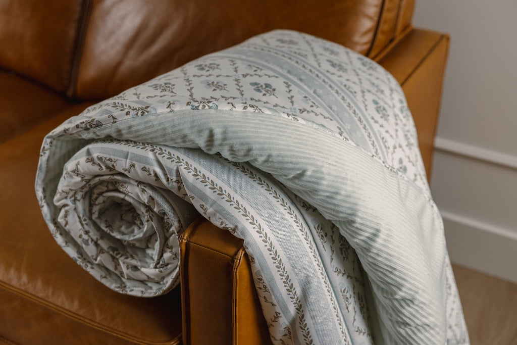 A blue floral and light blue corduroy blanket on an orange leather couch.