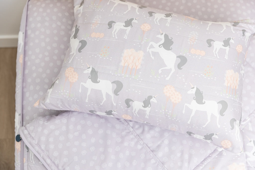 A twin bed made with purple unicorn kids zipper bedding, the top unzipped and slightly pulled back and a pillow on the bed.