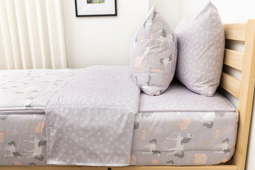 A side shot of a twin bed made with purple unicorn kids zipper bedding, the top unzipped and pulled back slightly and two pillows at the head of the bed