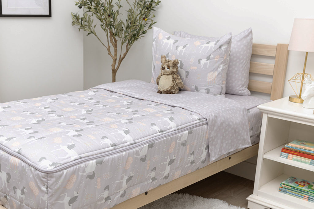 A twin bed made with purple unicorn kids zipper bedding, a nightstand beside it with books on the shelf and toys scattered on the floor