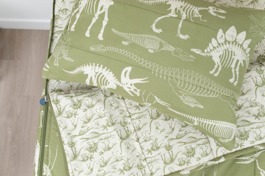 A twin bed made with olive green dinosaur fossils kids zipper bedding, the top unzipped and slightly pulled back and a pillow on the bed.