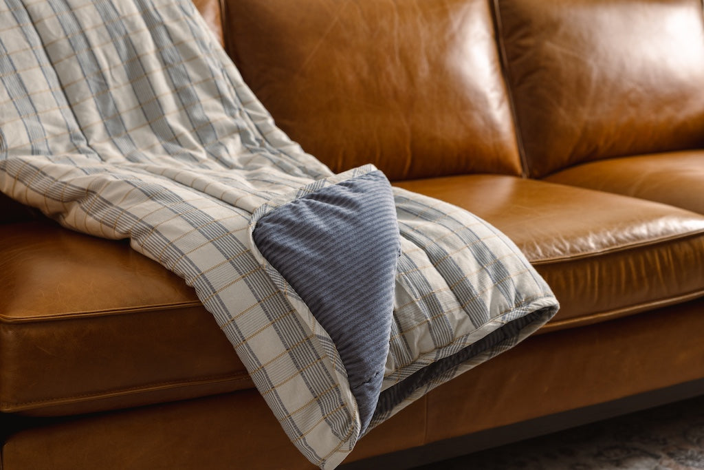 A blue and yellow plaid stitched blanket with a blue corduroy interior on an orange leather couch.