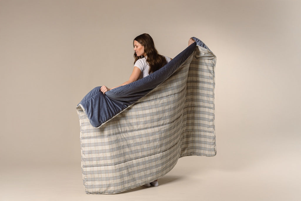 A model holding a blue and yellow plaid stitched blanket with a blue corduroy interior on a cream backdrop.