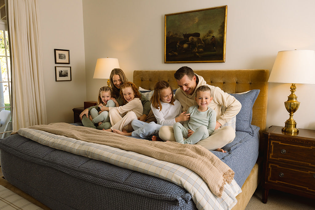 A family snuggling on blue textured bedding with tan and plaid accessories. 