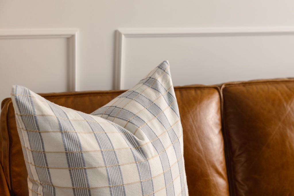 A yellow and blue plaid stitched pillow on a leather couch.