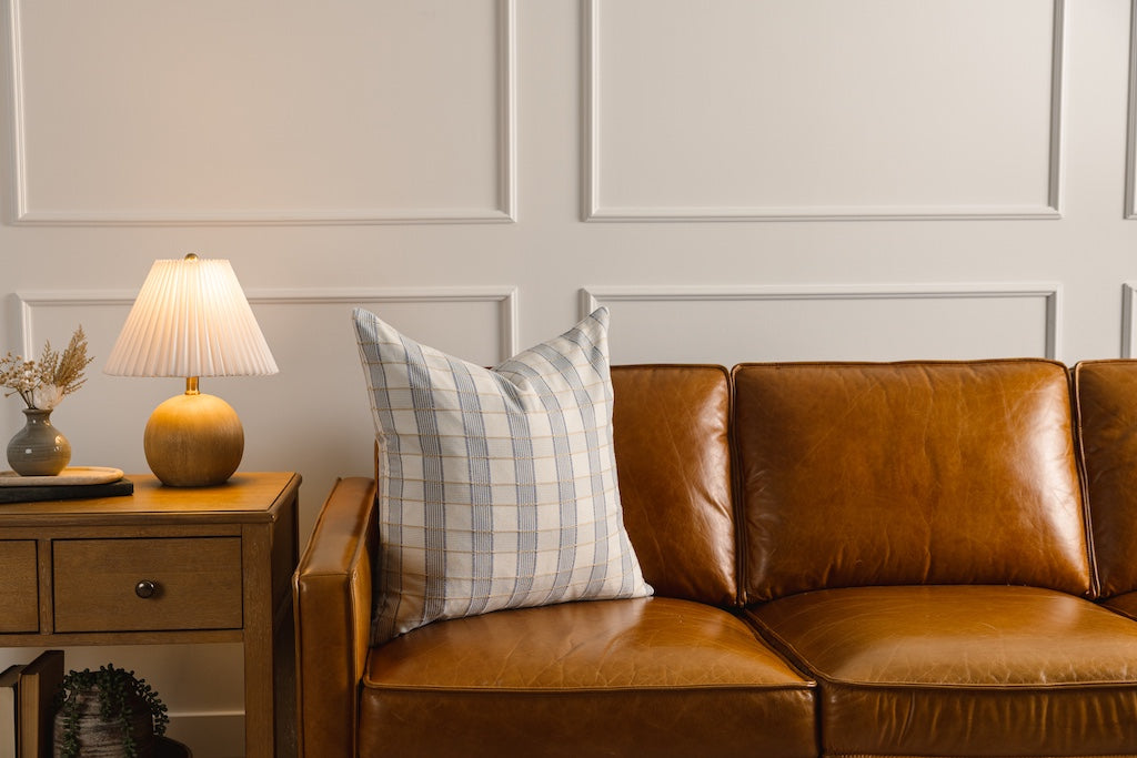 A yellow and blue plaid stitched pillow on a leather couch.