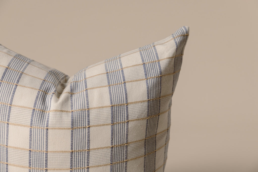 A yellow and blue plaid stitched pillow on a cream backdrop.