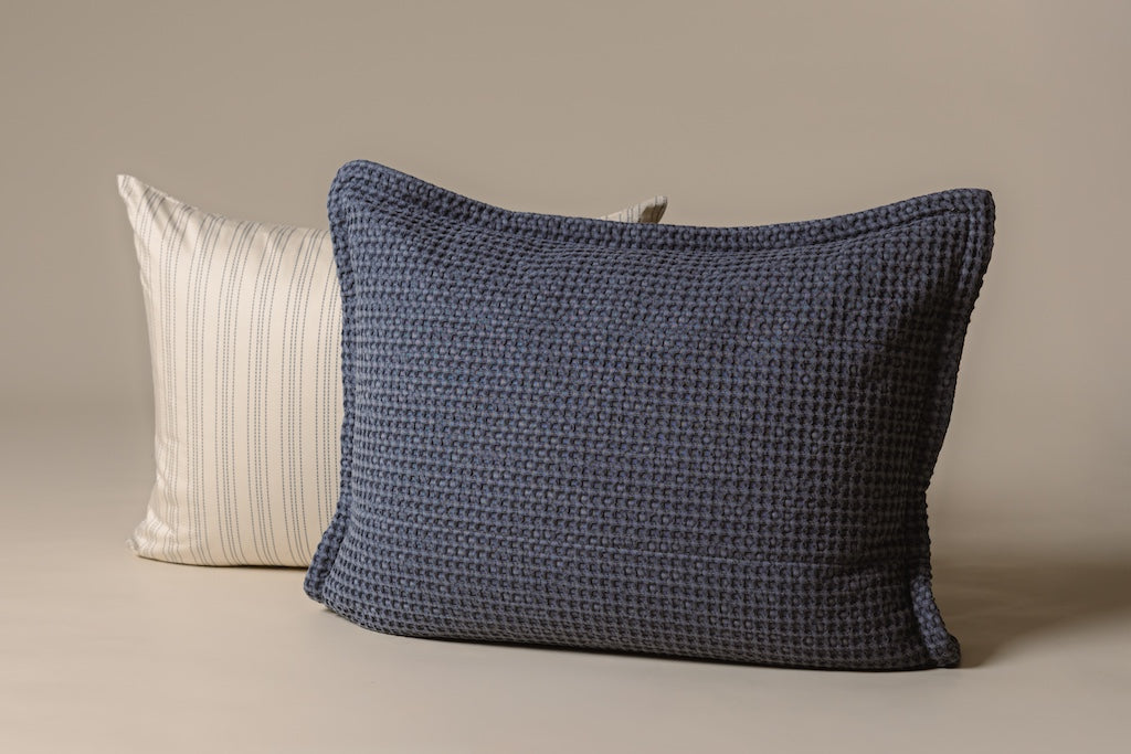 A cream and blue striped pillow and blue waffle textured sham on a cream backdrop.