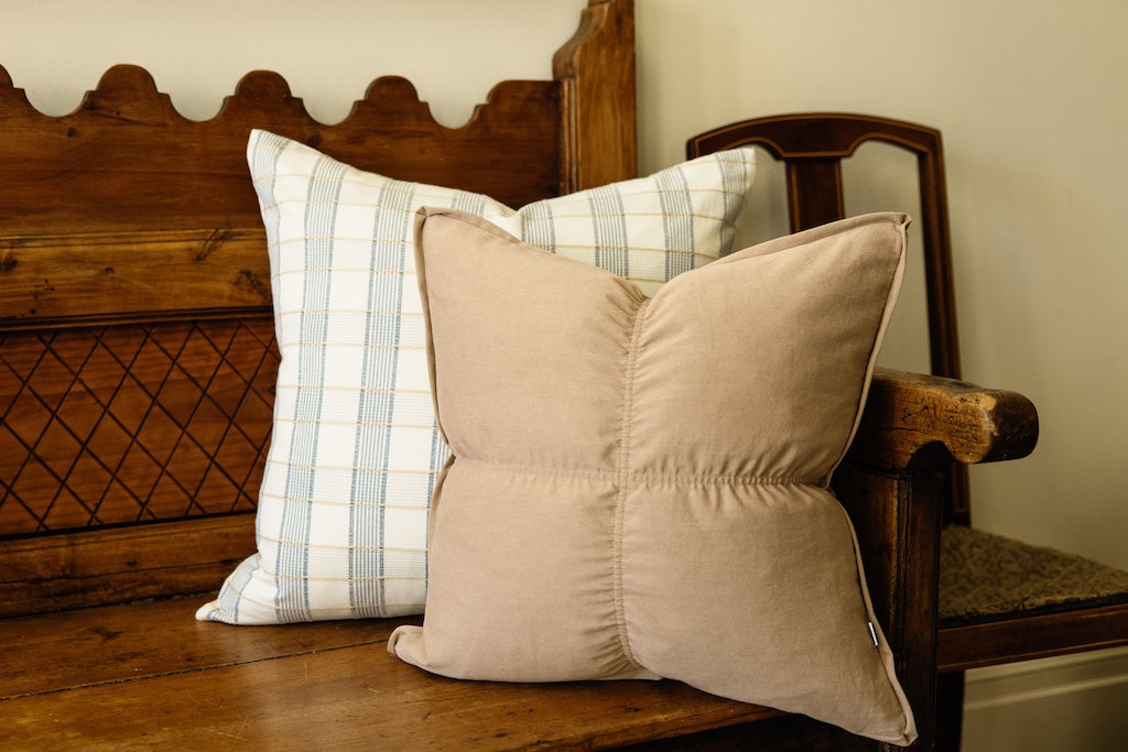 A light brown pillow with a blue and yellow plaid stitched pillow on a wood bench.