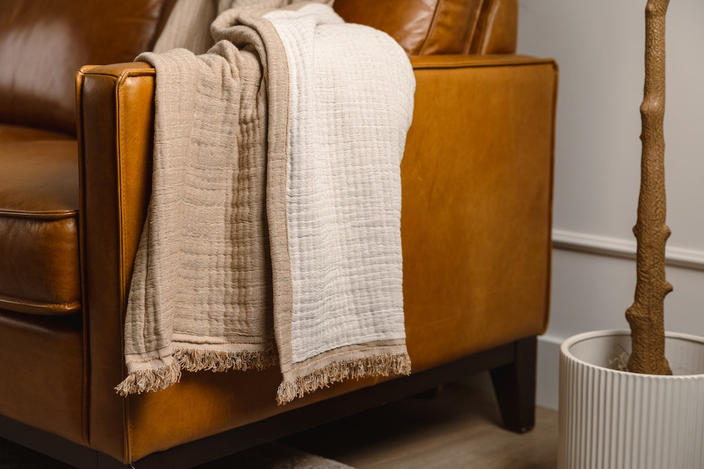 A light brown and cream with a fringed edge throw on an orange leather couch.