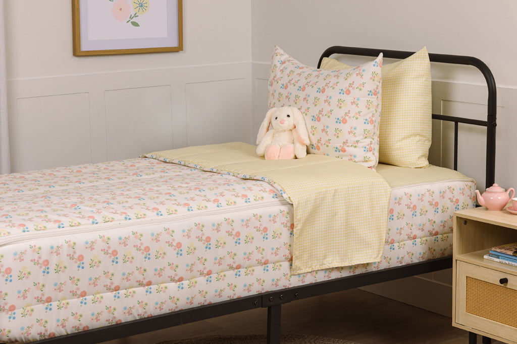 Children's zipper bedding in a bedroom on a black bed frame that has a flower print exterior and yellow gingham print interior, with a stuffed toy laying against the pillow.