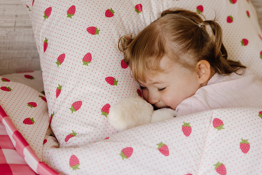 A young girl sleeping in pink gingham and strawberry print bedding.