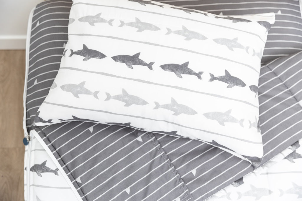 A twin bed made with shark kids zipper bedding, the top unzipped and pulled slightly back and a pillow on top
