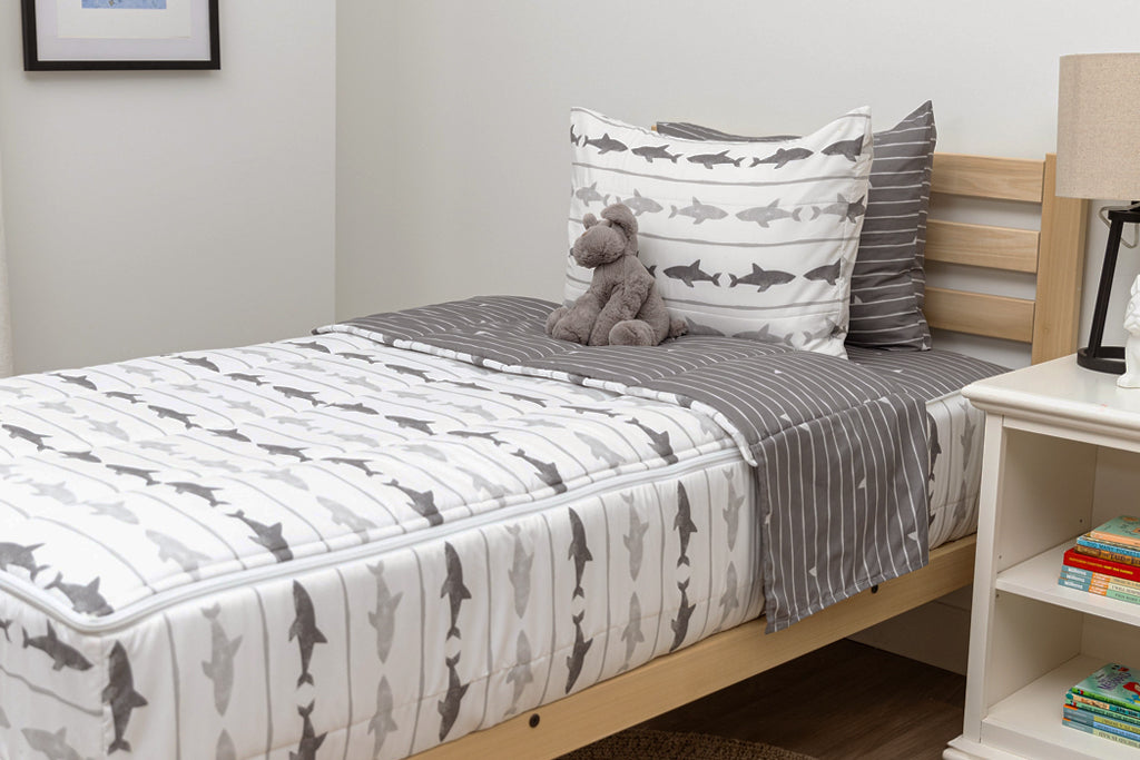 A twin bed made with shark kids zipper bedding, a nightstand next to it with books and toys strewn on the floor