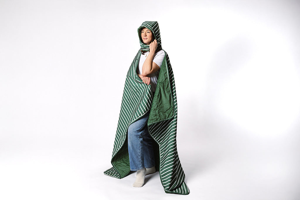 A woman wearing a green and white striped stadium blanket with a hood on a white backdrop.