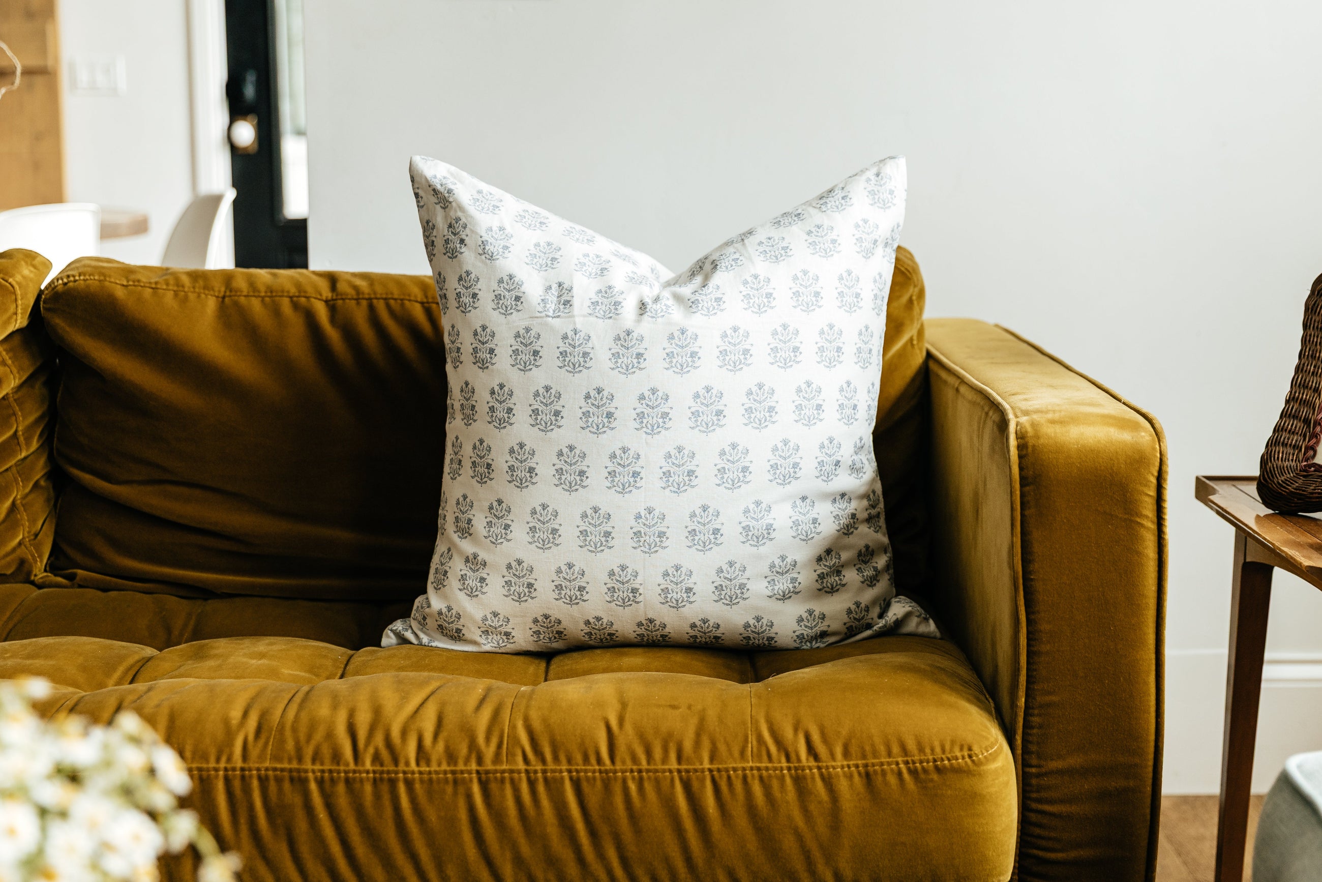 A white euro pillow with a blue floral design arranged on a mustard yellow velvet couch.