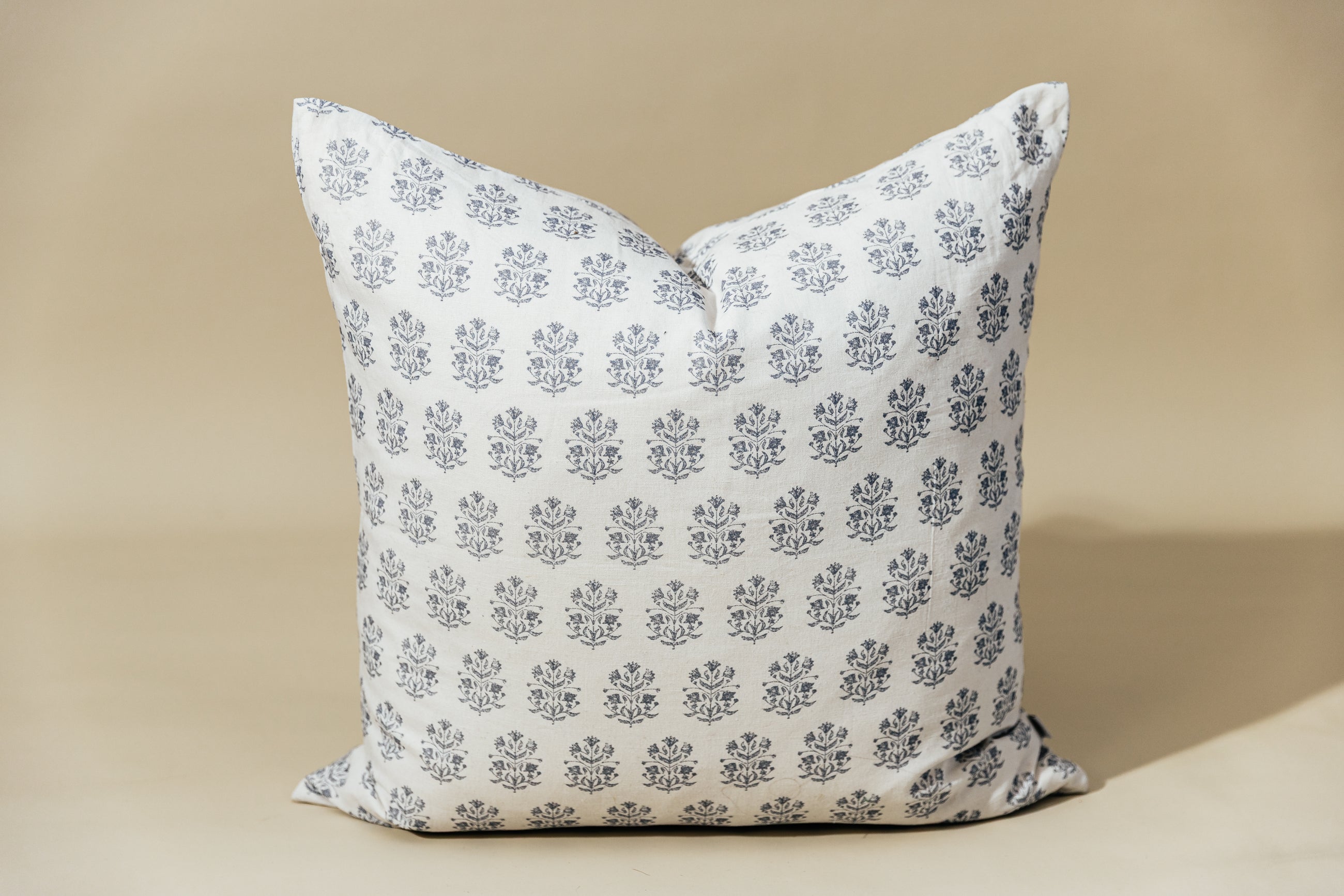 A white euro pillow with a blue floral design arranged on a tan background.