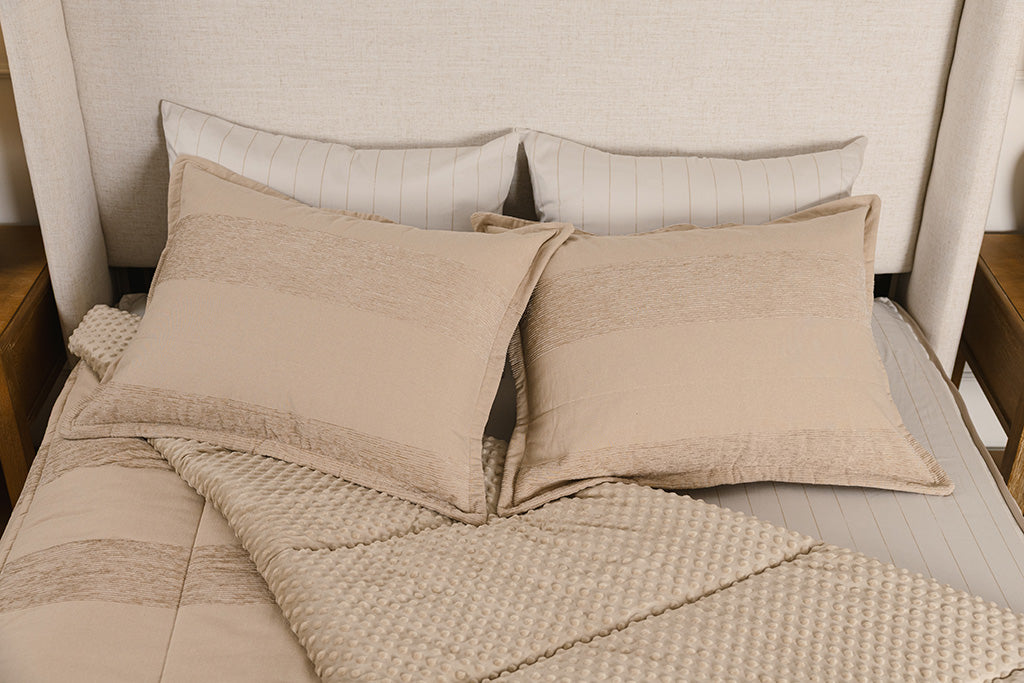A bed made with tan faded stripes zipper bedding with the comforter pulled back and pillows on top of the bed.