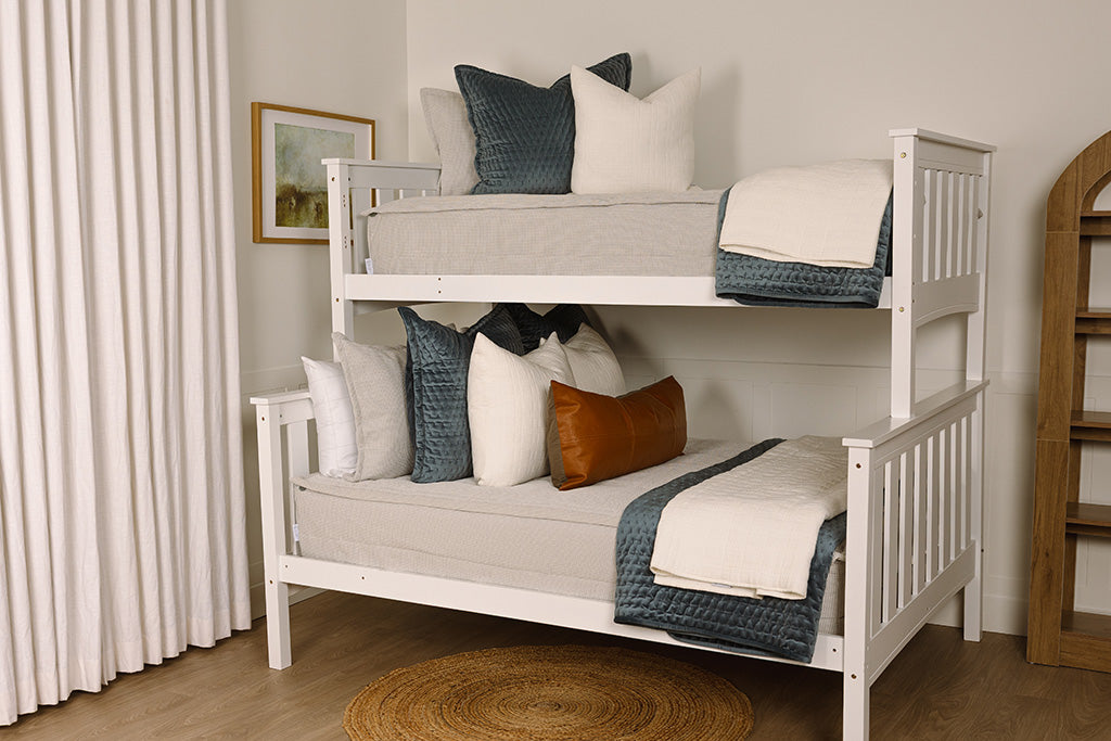 A bunk bed made with light gray waffle texture zipper bedding and an assortment of neutral and velvet blue blankets and accessories. 