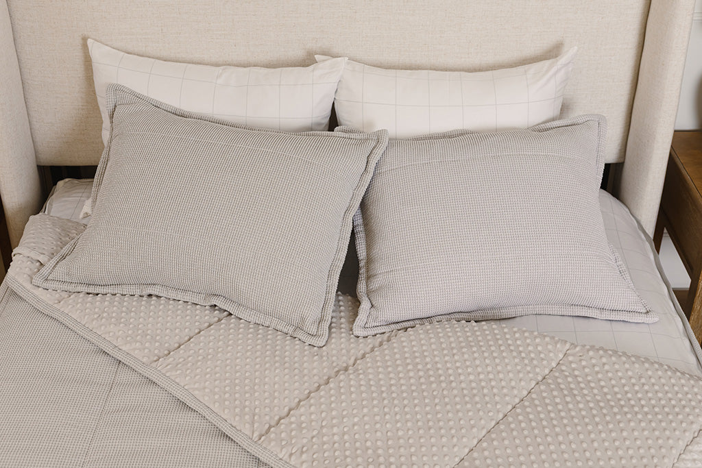 A bed made with light gray waffle textured zipper bedding with the comforter pulled back and pillows on top of the bed.
