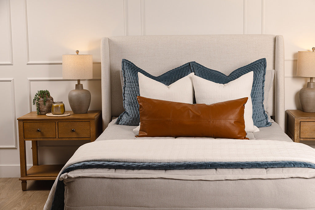 A bed made with light gray waffle texture zipper bedding and an assortment of neutral and velvet blue blankets and accessories. 