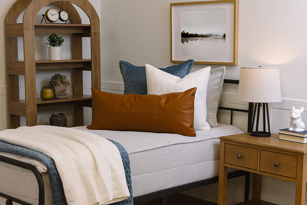 A twin bed made with light gray waffle textured zipper bedding and an assortment of black striped and neutral pillows and blanket.