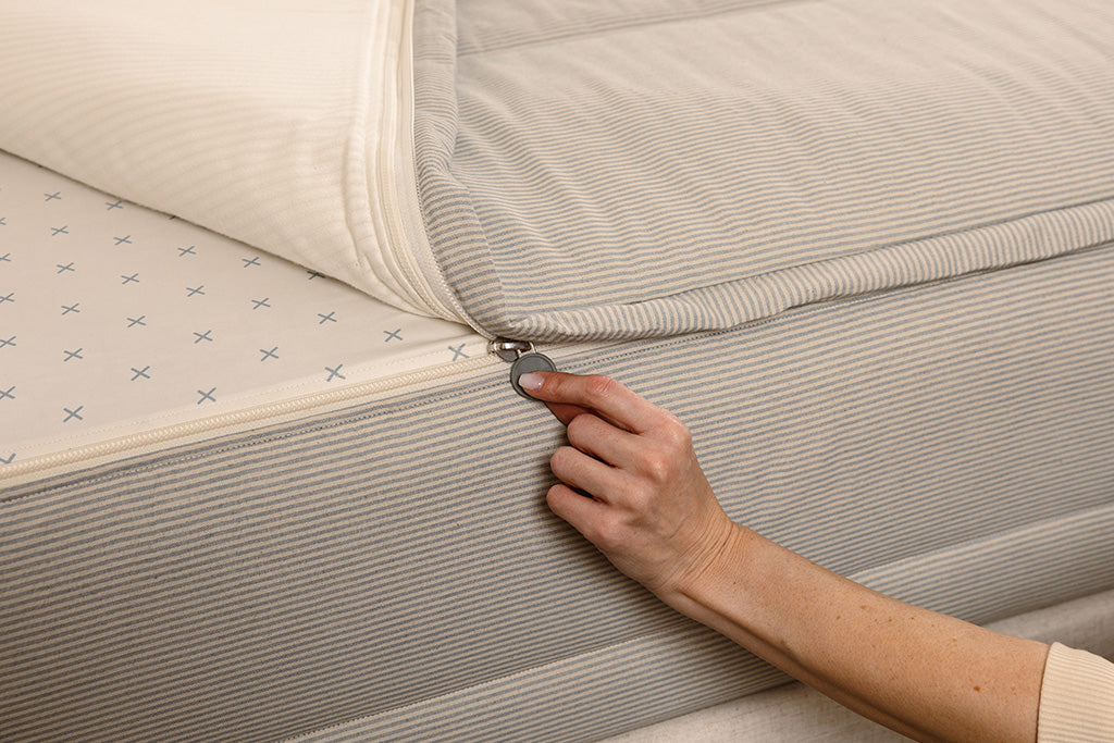 A close up photo of a zipper being pulled on blue and white striped zipper bedding.