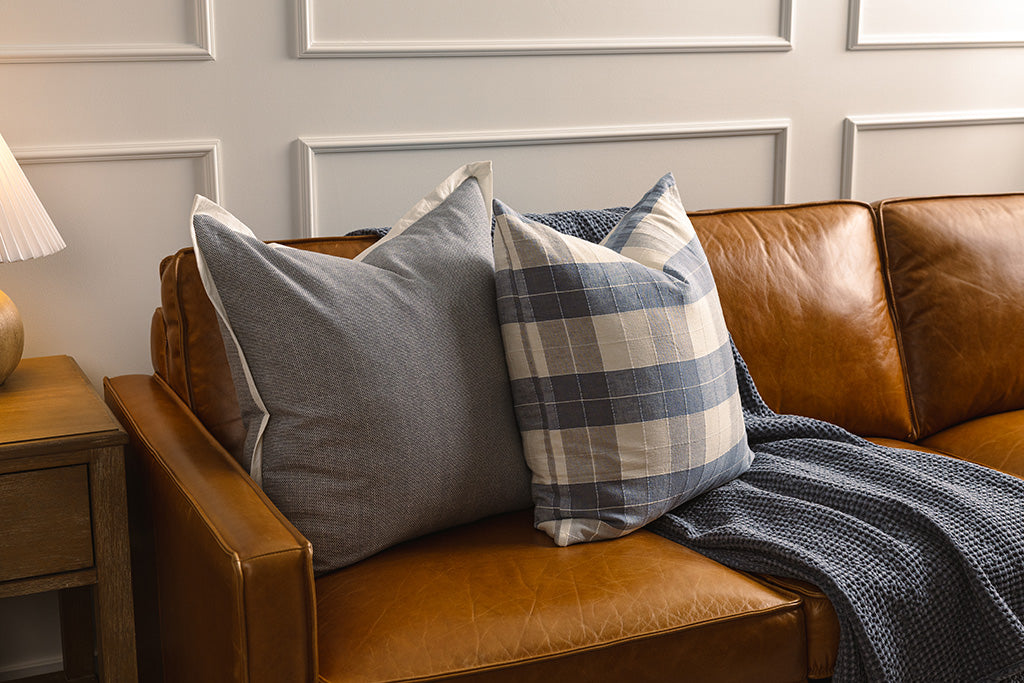 Blue and plaid accessories on an orange leather couch. 