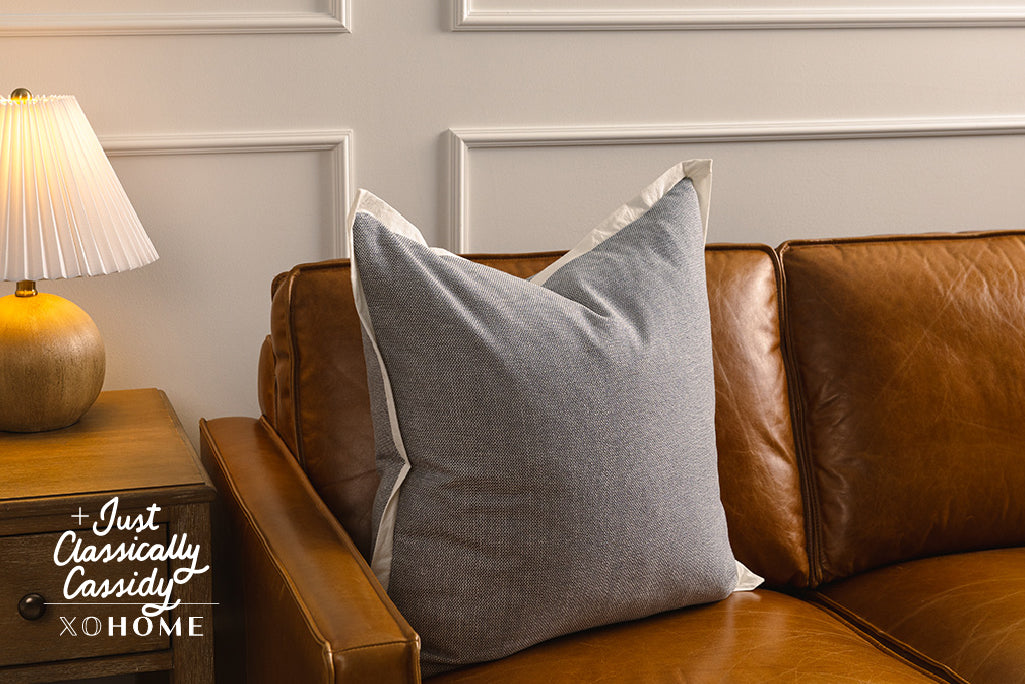 A light blue pillow with a cream trim on an orange leather couch.