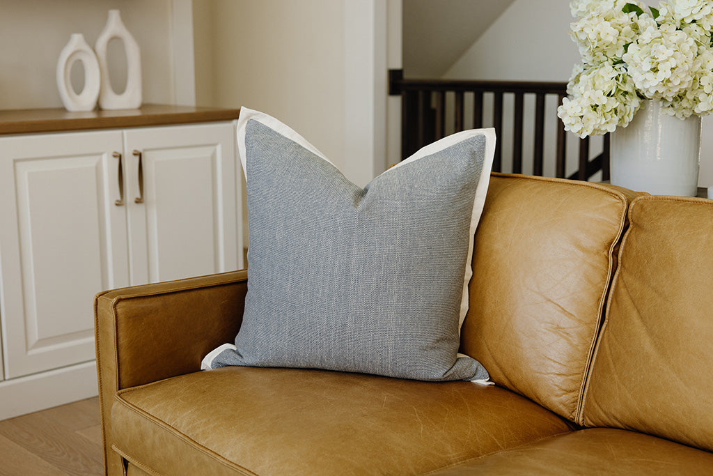 A light blue pillow with a cream trim on yellow leather couch.