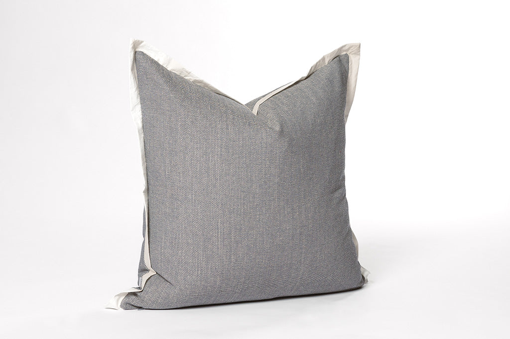 A light blue pillow with a cream trim on a white backdrop.